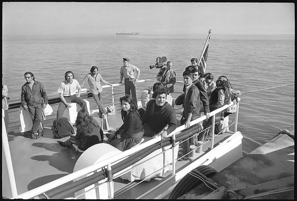 Black and white photograph of Richard Oakes and AIM members on a boat in San Francisco Bay approaching Alcatraz.