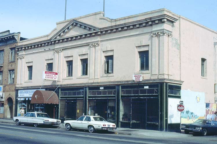 Color photograph of a beige building in an urban location, late 1960s. Cars of the era are parked in front of the building. The words ”American Indian Center” are printed on two signs hanging on the building.
