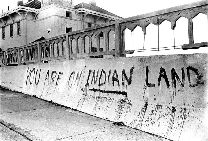 Black and white photograph of 'You are on Indian Land' painted on a concrete wall at Alcatraz.