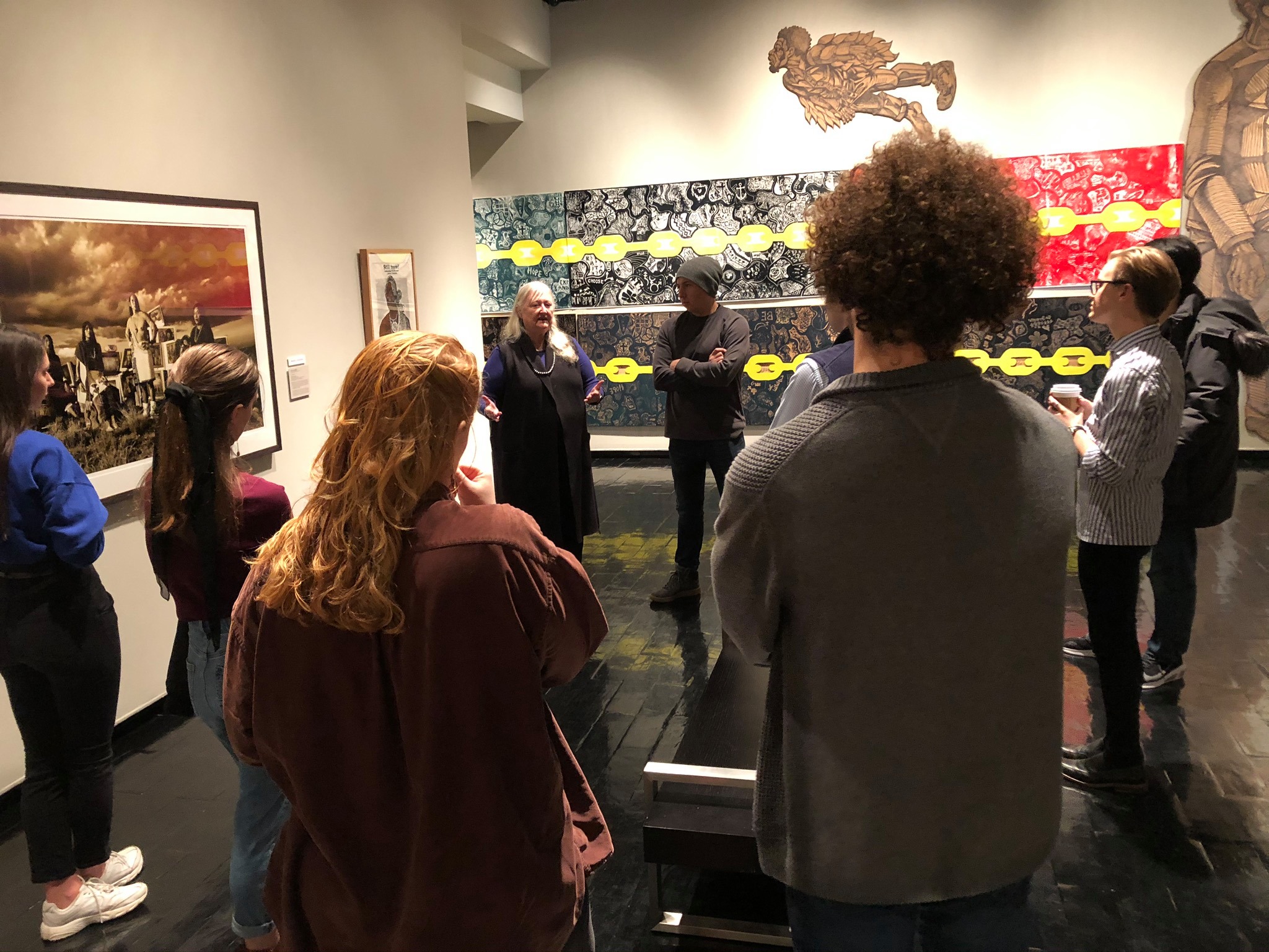 Color photograph of the author Tommy Orange meeting with a group of seven students from the Native Sovereignty seminar in a gallery at the Muscarelle Museum of Art during January 2020. Professor Danielle Moretti-Langholtz and Tommy Orange appear in the back center of the image. 
