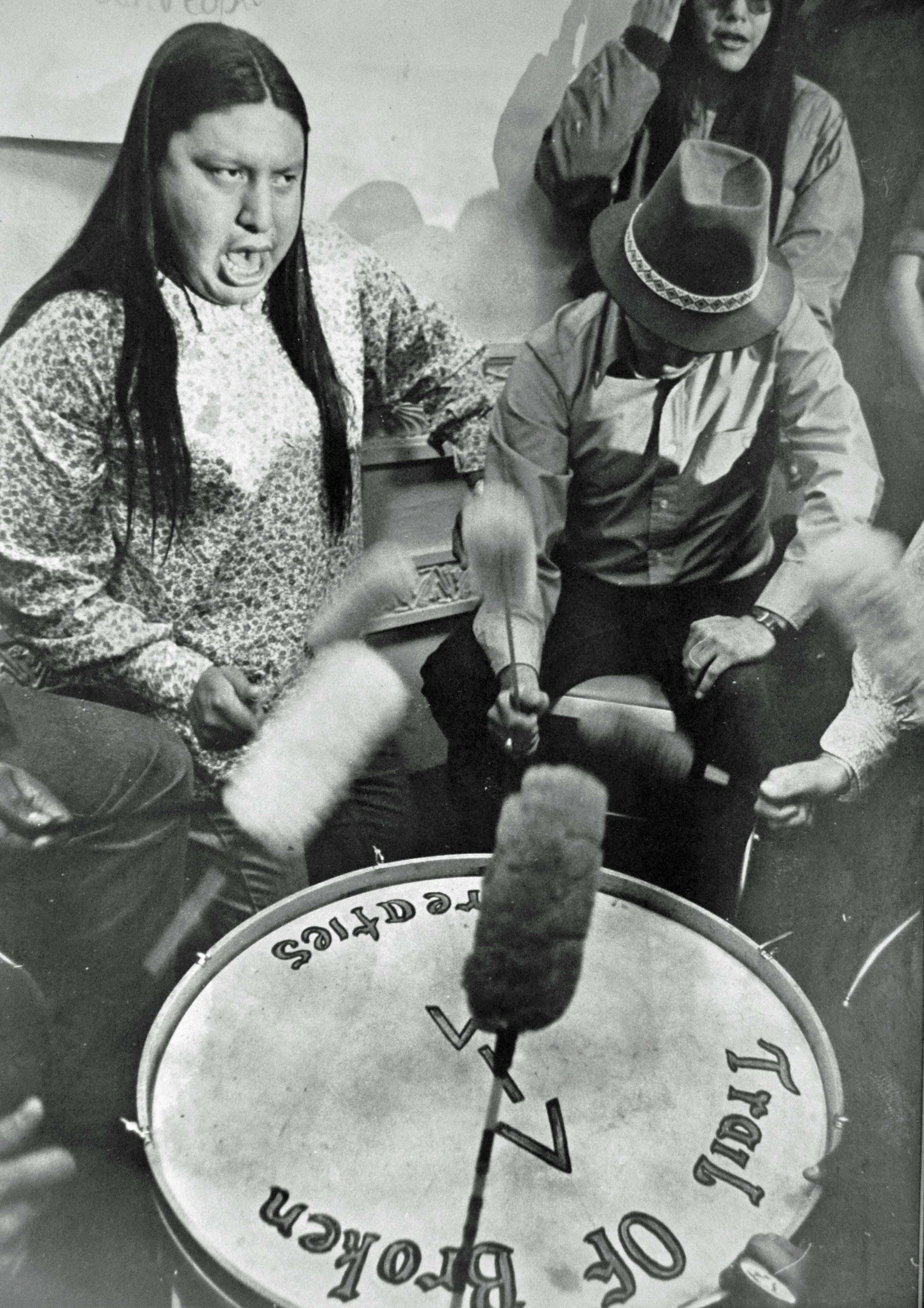 Black and white photograph of a Native American man leading a drum session in the Bureau of Indian Affairs in Washington, D.C. on the first day of demonstrations. 